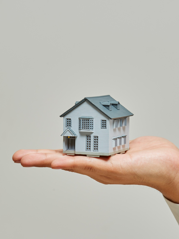 Hand holding a model house, representing Shared Ownership staircasing and buying a larger share of your home.